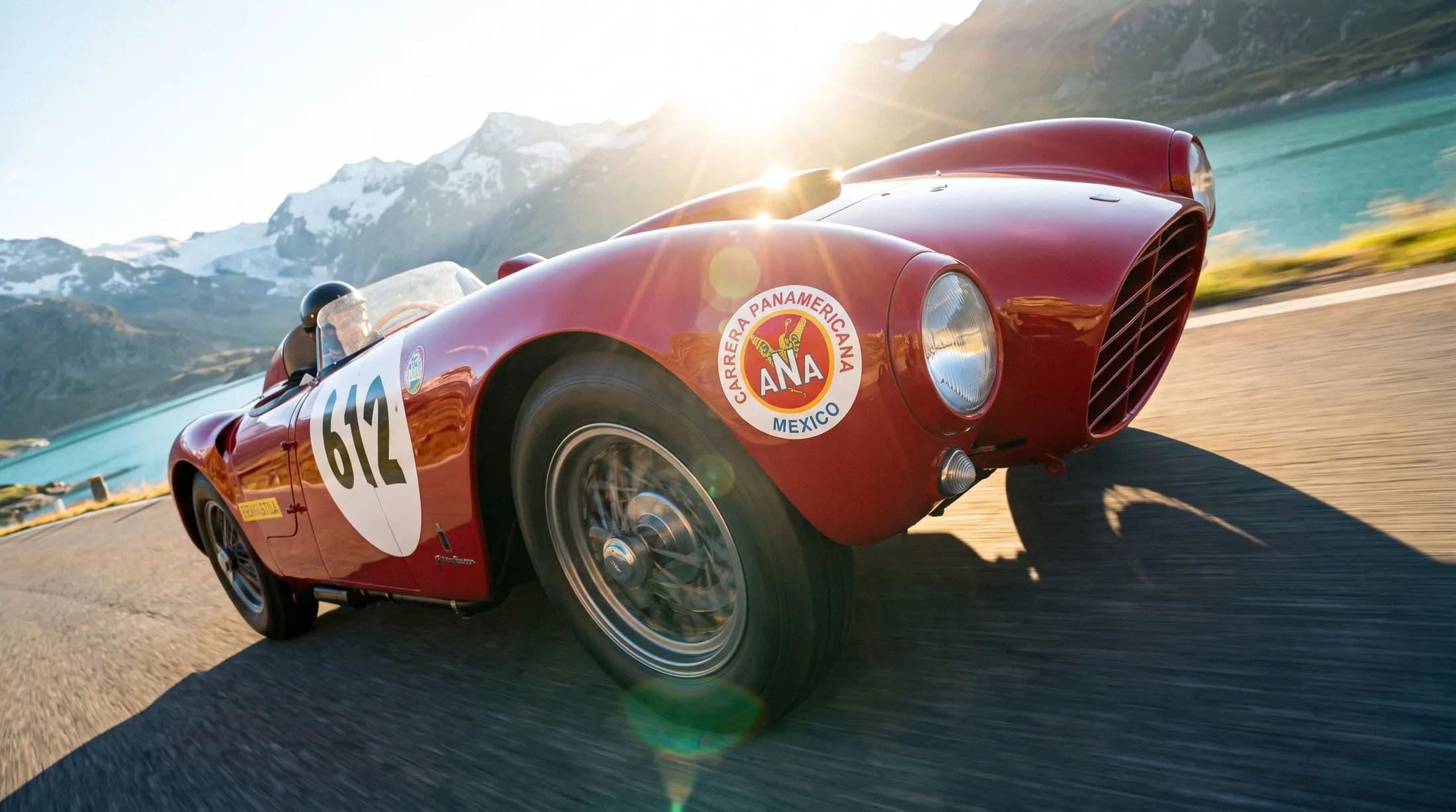 A red classic racing car on a mountain pass with a lake behind it